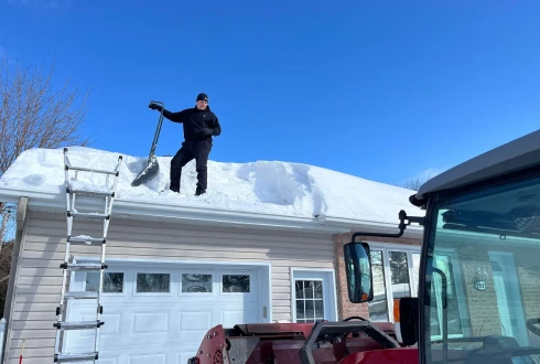 Un employé de À Point Déneigement en train de déneiger le toit d’une maison.